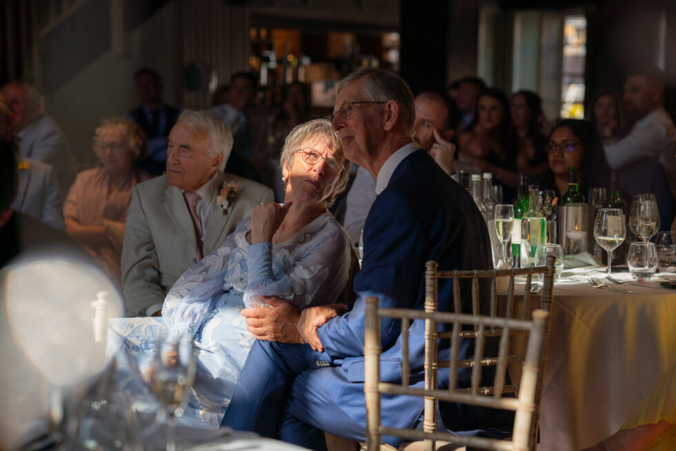 Emotional moment between the groom's grandparents showing deep affection and embracing at their table during the wedding breakfast. Captured by an authentic documentary Hertfordshire wedding photographer.