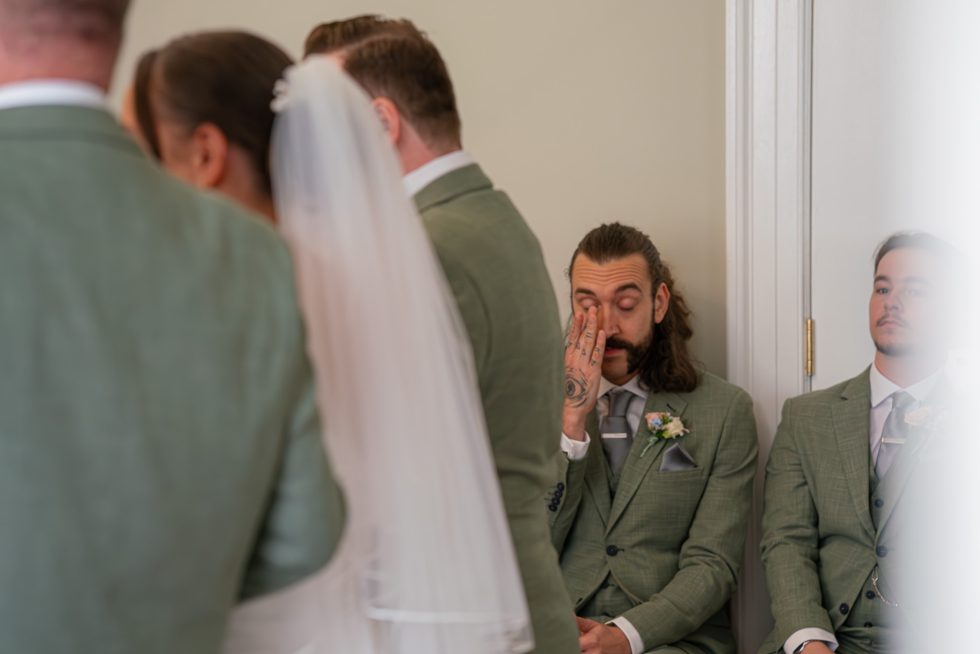 Candid photo of the groom's best man getting emotional and wiping away a tear as the bride joins the groom at the altar. Documentary style photography by an experienced Hertfordshire wedding photographer.