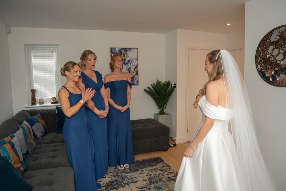 The emotional moment the bride reveals her dress to her bridesmaids, capturing their joyful reactions during the getting ready phase. Candid photography by a Bedfordshire wedding photographer.