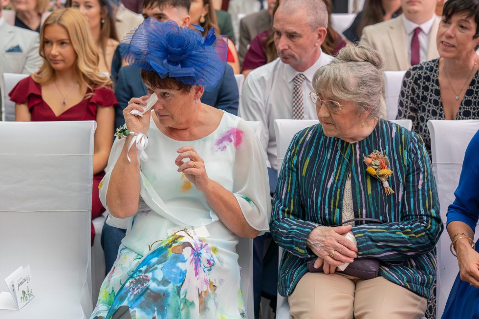 Candid photo of the Mother of the Bride crying happy tears during the wedding ceremony while being comforted by the Grandmother of the Bride.
