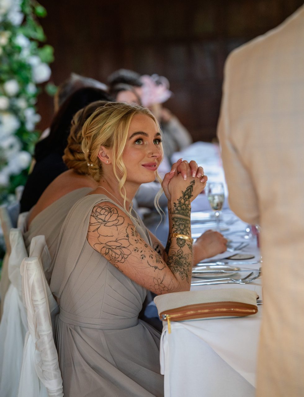 A bridesmaid captivated and enjoying the Best Man's speech during the wedding breakfast at the luxury Great Fosters Hotel. Candid, documentary photography by a Hertfordshire wedding photographer.