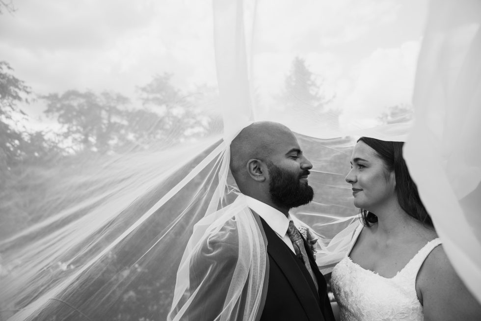 A beautiful black and white, intimate portrait of the bride and groom looking at each other beneath the veil, symbolizing the fusion of Indian and English cultures. Captured by a romantic Hertfordshire wedding photographer.