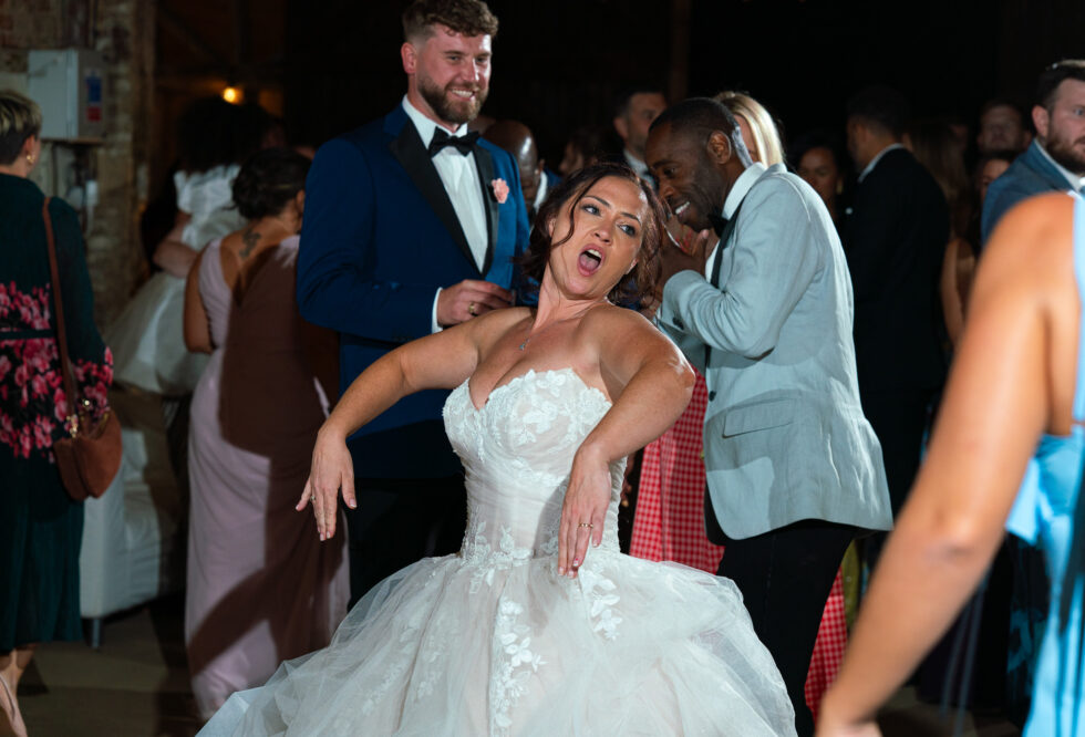 Bride pulling a playful dance move on the dancefloor at her Hertfordshire wedding reception
