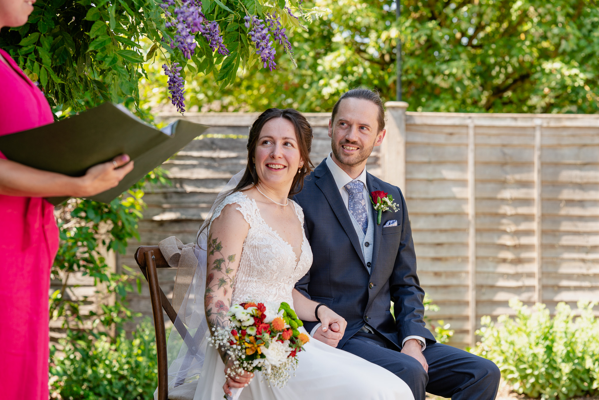 Bride and groom smiling during outdoor garden wedding ceremony, friend officiant reading vows