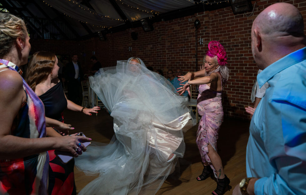 Bride's veil flying as she dances on the dancefloor, surrounded by guests at wedding reception