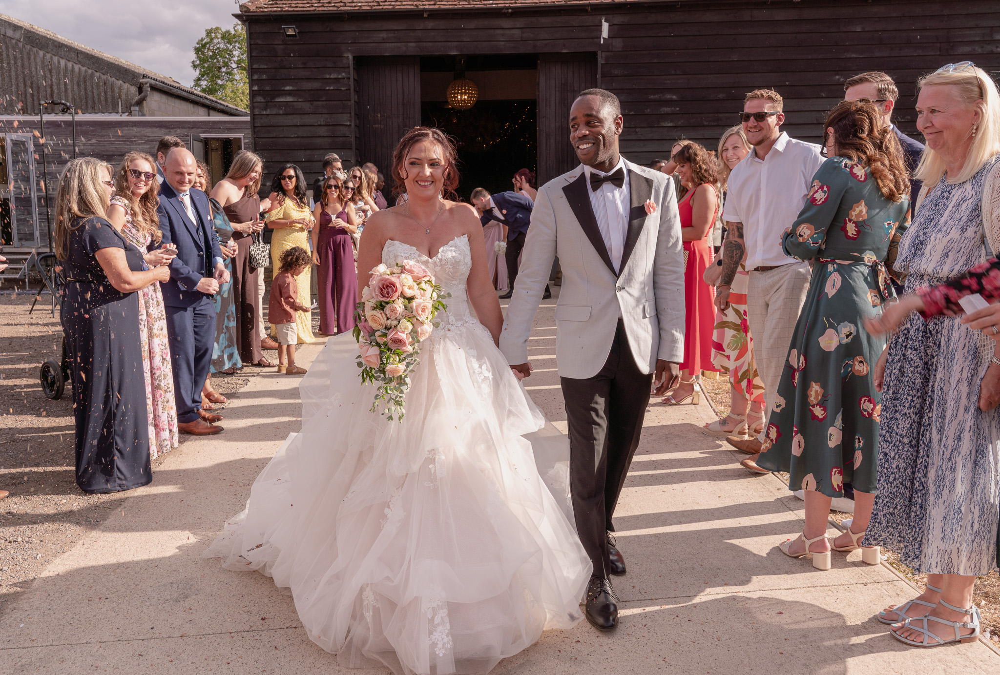 Bride and groom walking hand in hand through confetti line outside barn wedding venue in Hertfordshire