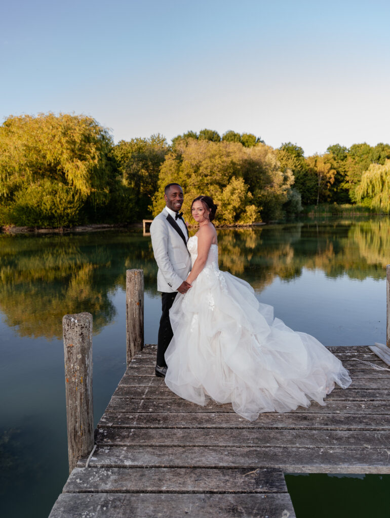 Groom kissing his bride on the forehead on a wooden jetty beside a lake