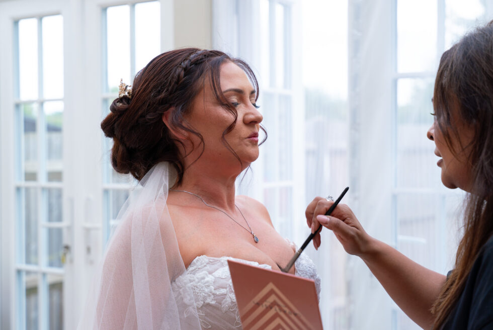 Bride in her veil having her makeup finished on the morning of the wedding