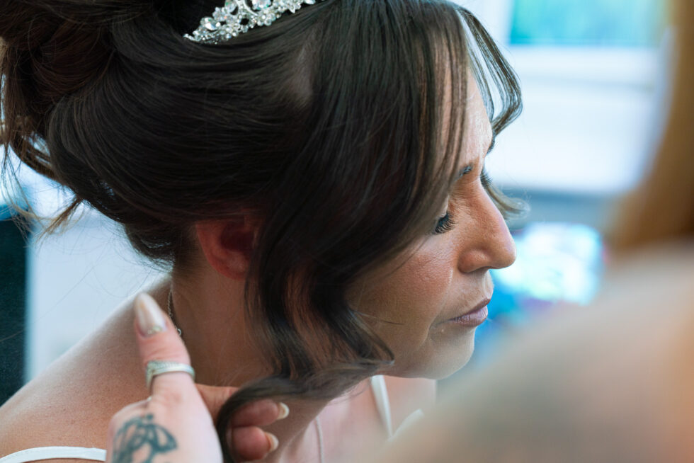 Close-up side profile of a bride in a tiara looking down while someone helps with her getting-ready details