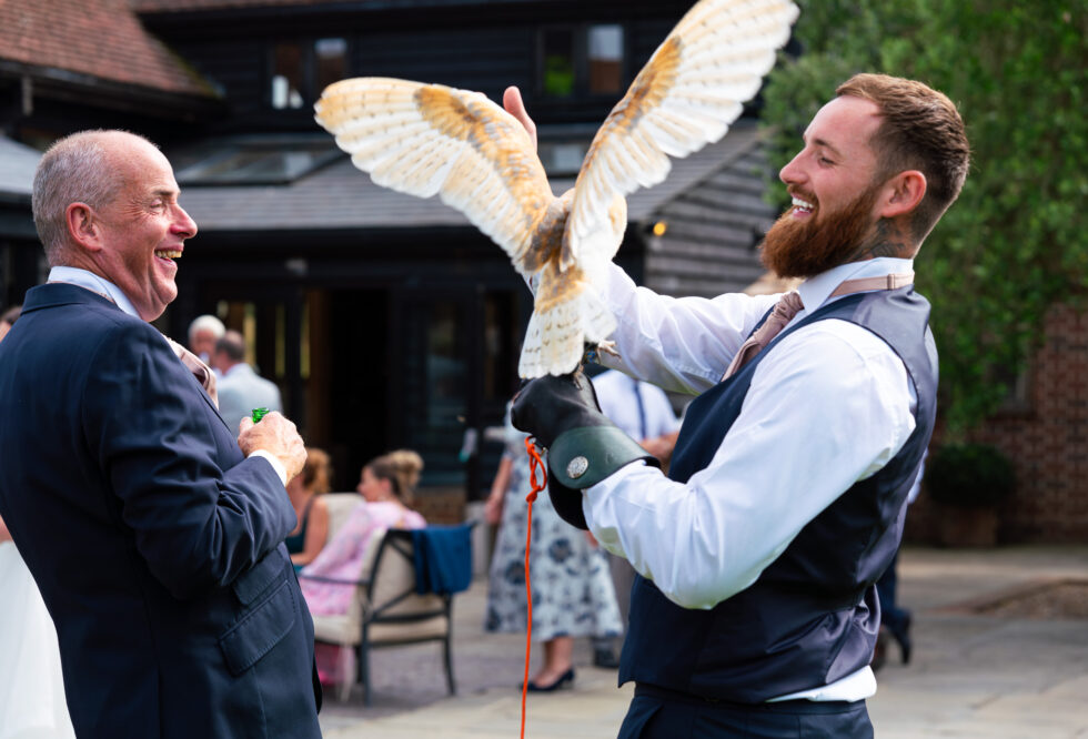 Falconer holding a barn owl with wings spread at a wedding venue