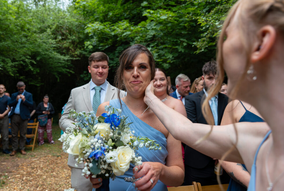 Wedding guest in blue smiling while another guest fusses beside her with a bouquet