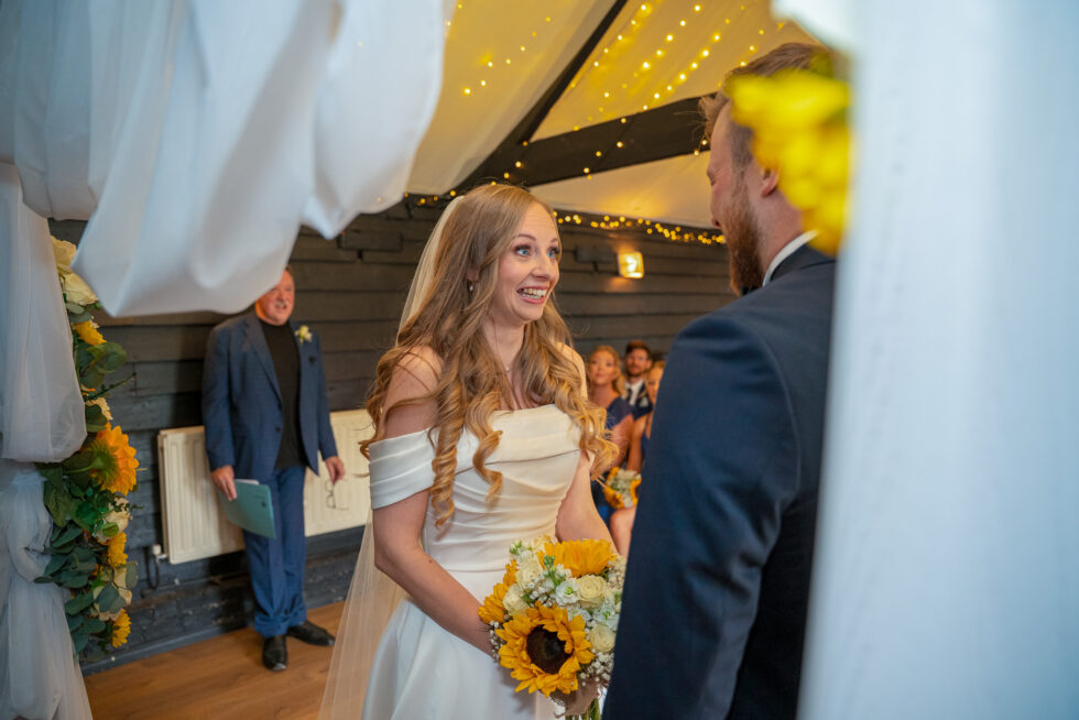 Bride smiling at her partner holding a sunflower bouquet at the start of the ceremony