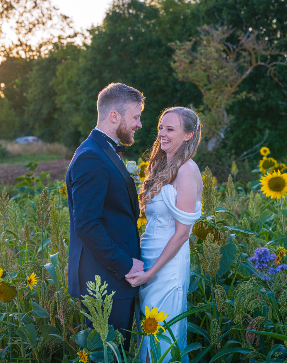 Bride and groom standing close together among sunflowers at golden hour