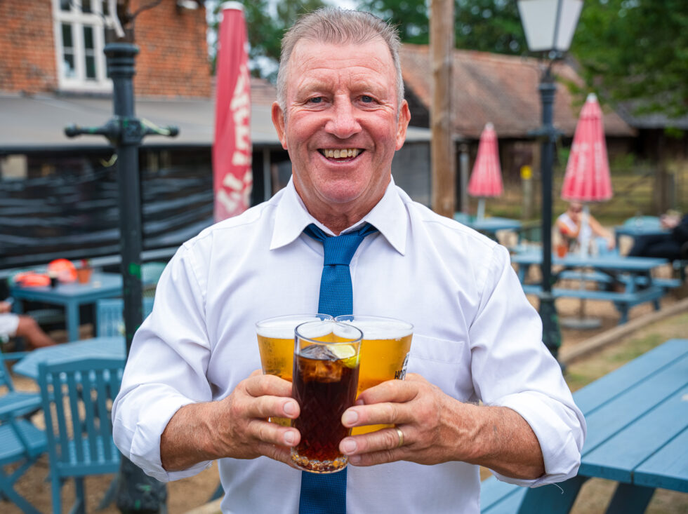 Smiling man in a white shirt and blue tie holding two pints of beer