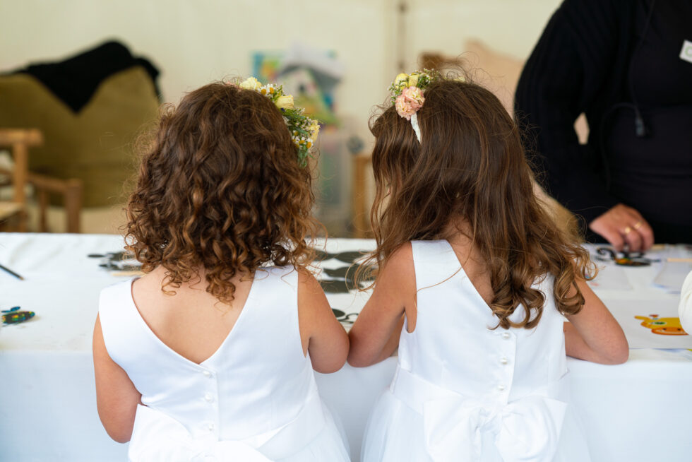 Two flower girls seen from behind in white dresses with flower crowns