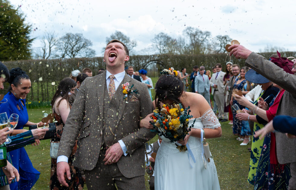 Groom laughing with his head back as confetti is thrown over the couple