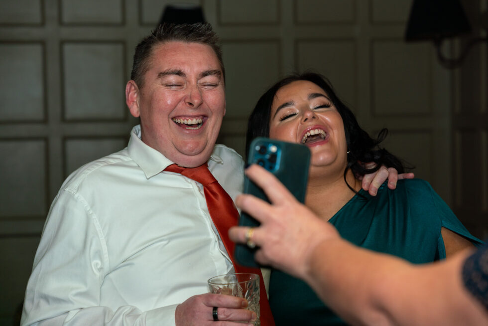 Wedding guests laughing together while taking a selfie on a phone