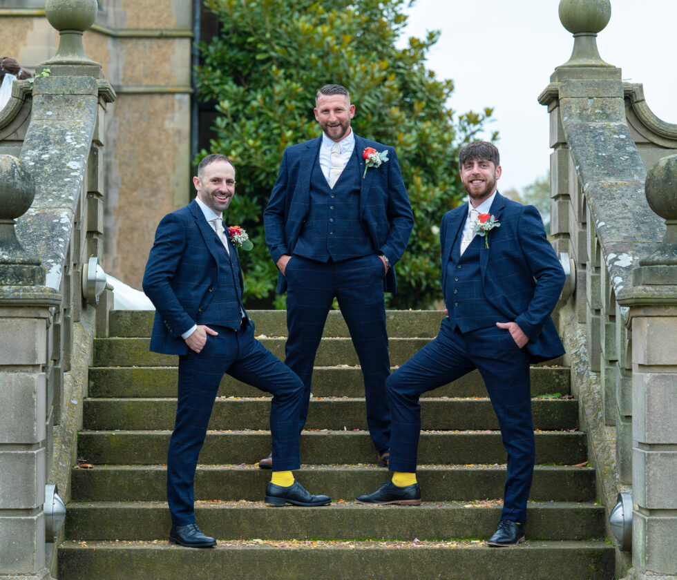 Groom and groomsmen standing relaxed on stone steps in blue suits