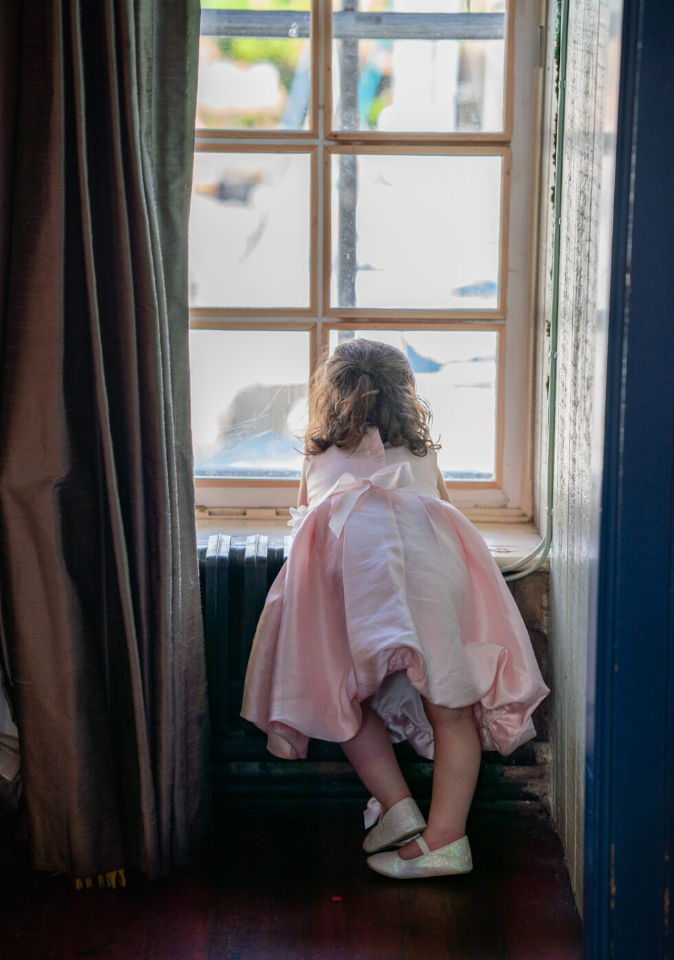 Small girl in a pink dress looking out of a window at a wedding