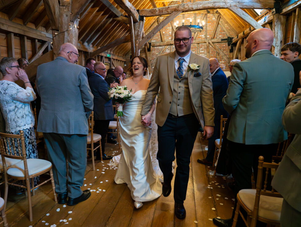Couple walking back down the aisle as confetti is thrown in a barn ceremony