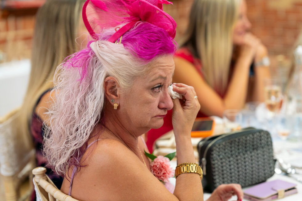 Wedding guest in a pink fascinator wiping away happy tears