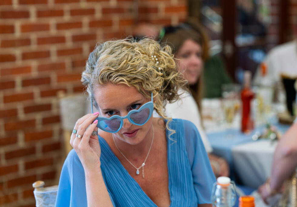 Wedding guest in blue laughing while wearing quirky sunglasses