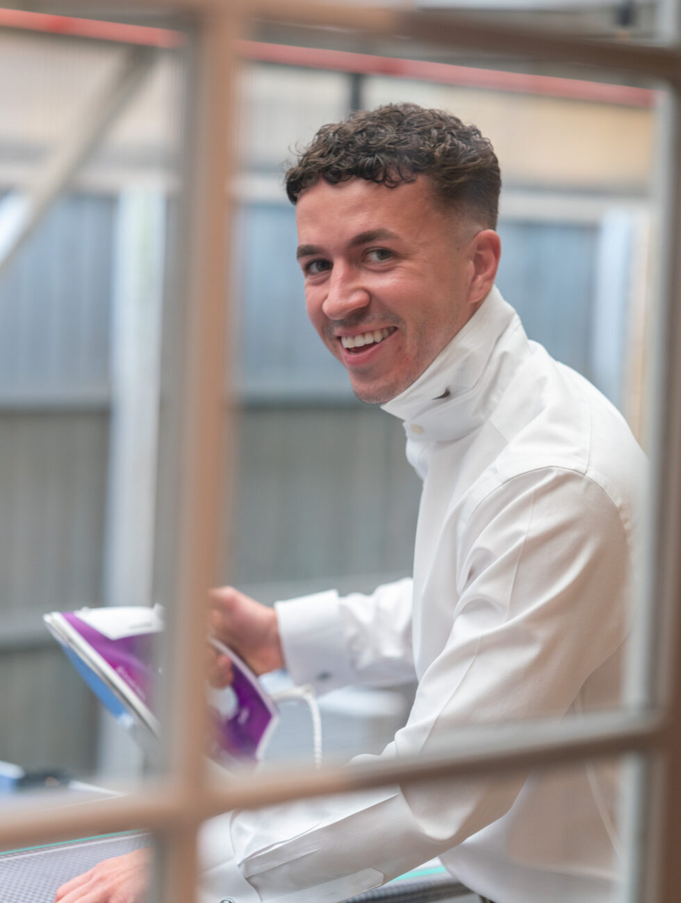 Groom in a white shirt smiling at the camera while getting ready