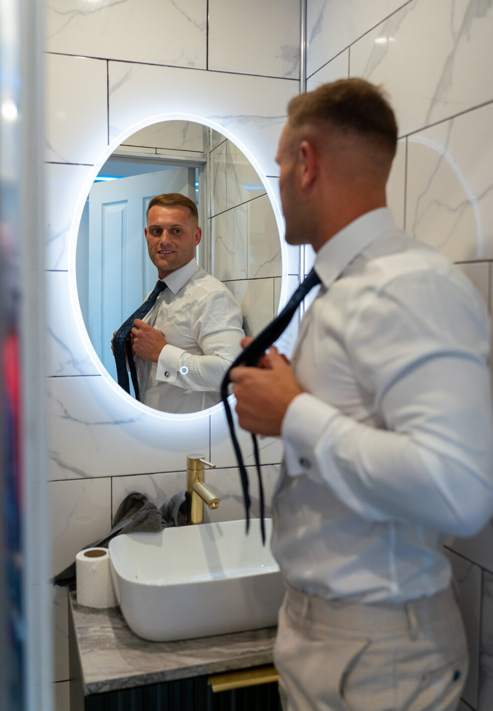 Groom and best man getting ready in front of a mirror, adjusting a tie