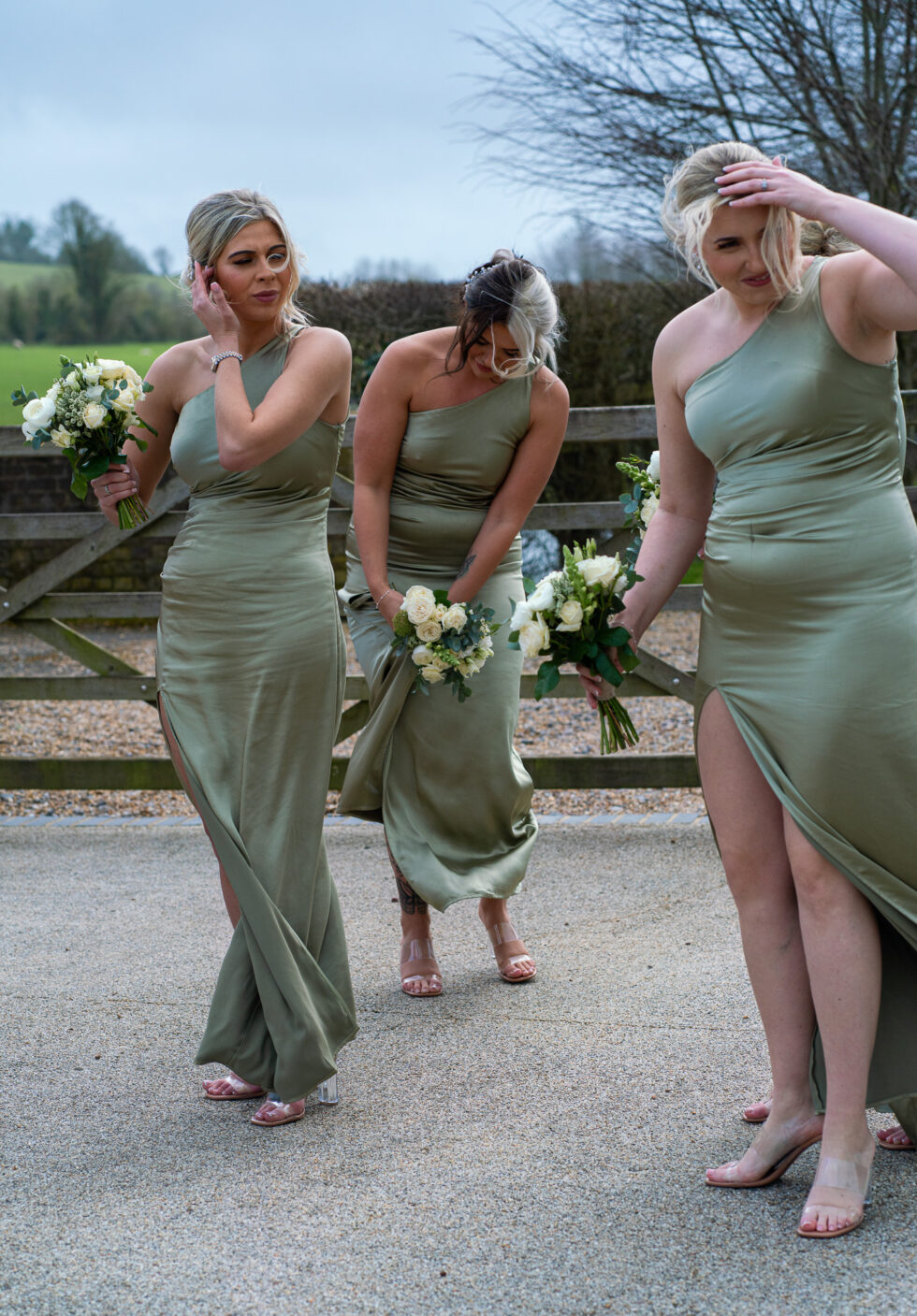 Bridesmaids in green dresses laughing and dancing along a path with bouquets