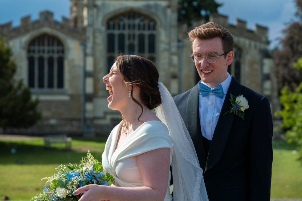 Bride laughing out loud beside her smiling groom in front of St Mary's Church, Hitchin