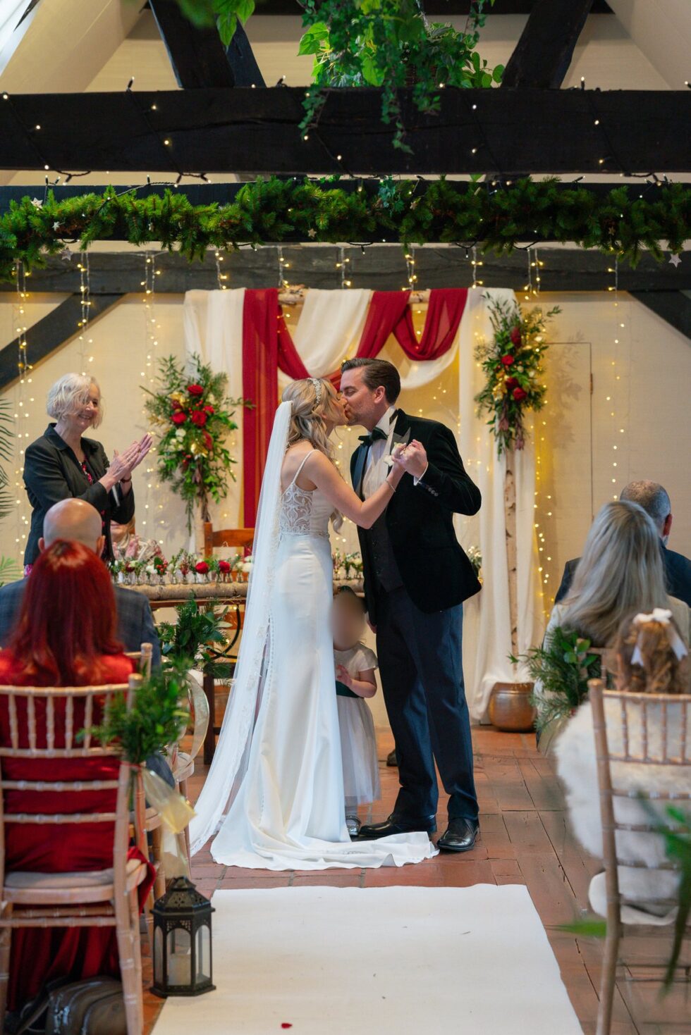 Couple sharing a first kiss during an indoor ceremony decorated with flowers and red drapes